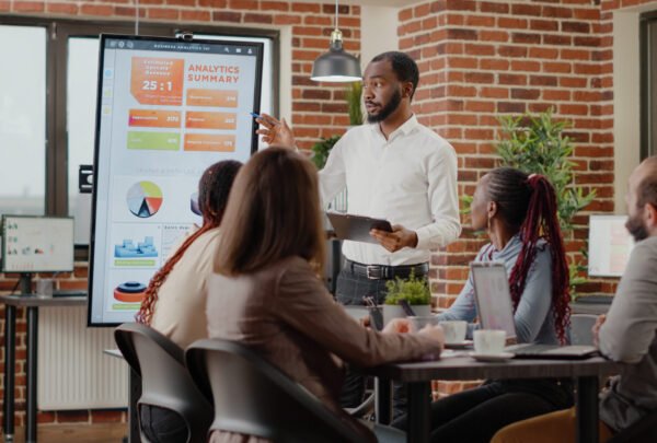 Company employee presenting business strategy with charts on monitor, planning project. Workmates analyzing financial statistics on display, working together on company development.