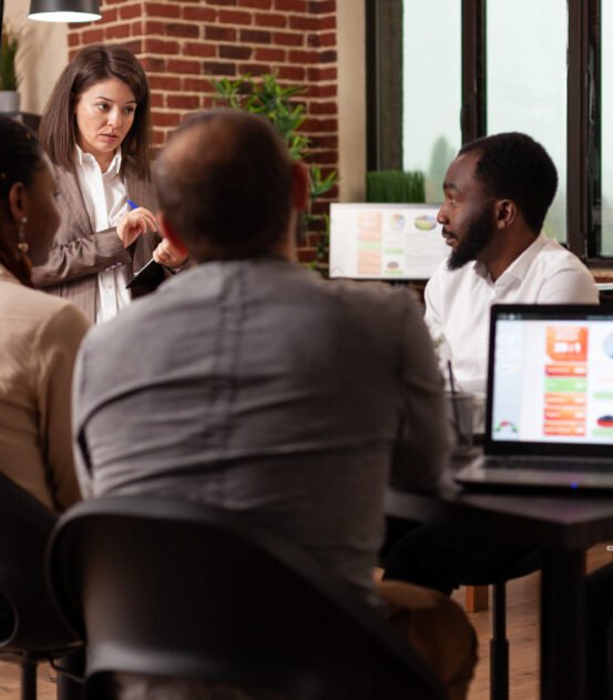 Executive manager explaining management presentation showing company strategy using monitor working at business project in startup office. Diverse team sitting at meeting table brainstorming ideas